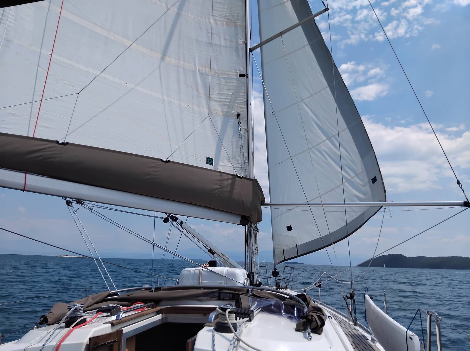 Segelyacht mit ausgebaumtem Vorsegel vor dem Wind auf offenem Meer